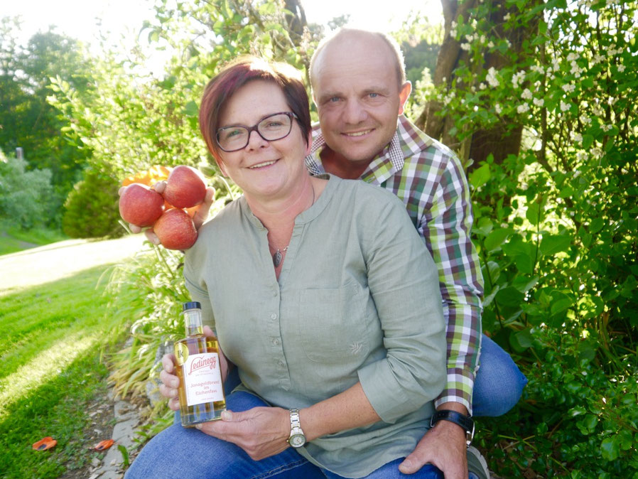 Gastgeber des Campingplatzes Obstgut Ledinegg präsentieren ihre hofeigenen Produkte: Frische rote Äpfel und selbstgebrannten Jonagoldbrand im Eichenfass.