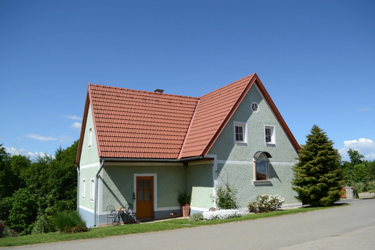 Außenansicht des freistehenden Ferienhauses am Obstgut Ledinegg in der Südsteiermark: Ein hell grünes Landhaus mit rotem Ziegeldach und kleiner Sitzgruppe vor dem Eingang.